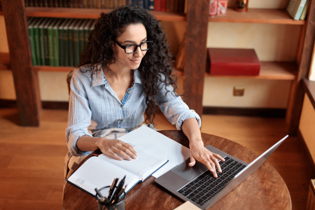 Mulher branca de cabelos pretos na frente do computador trabalhando com a intenção de ser mais produtiva.