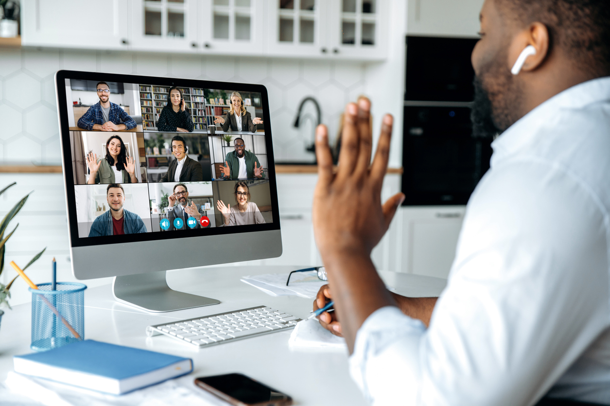 Homem negro conversando com sua equipe pelo computador, fazendo a liderança remota de um time.